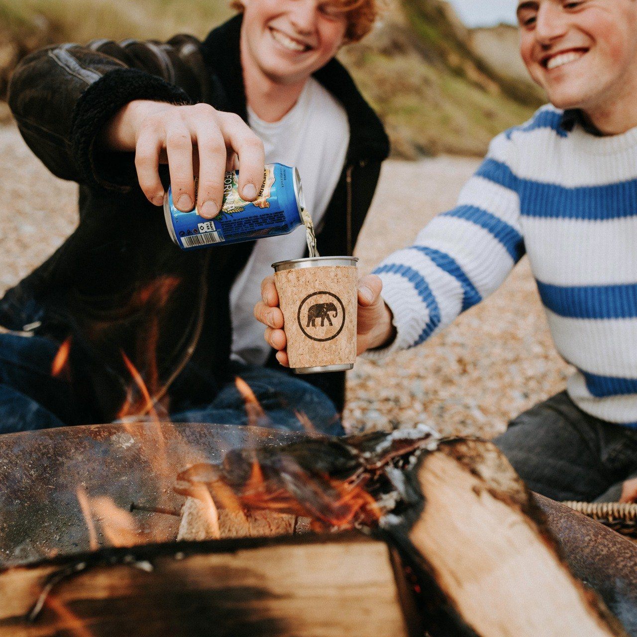 Reusable coffee cup on the beach with beer being poured into it over a fire.