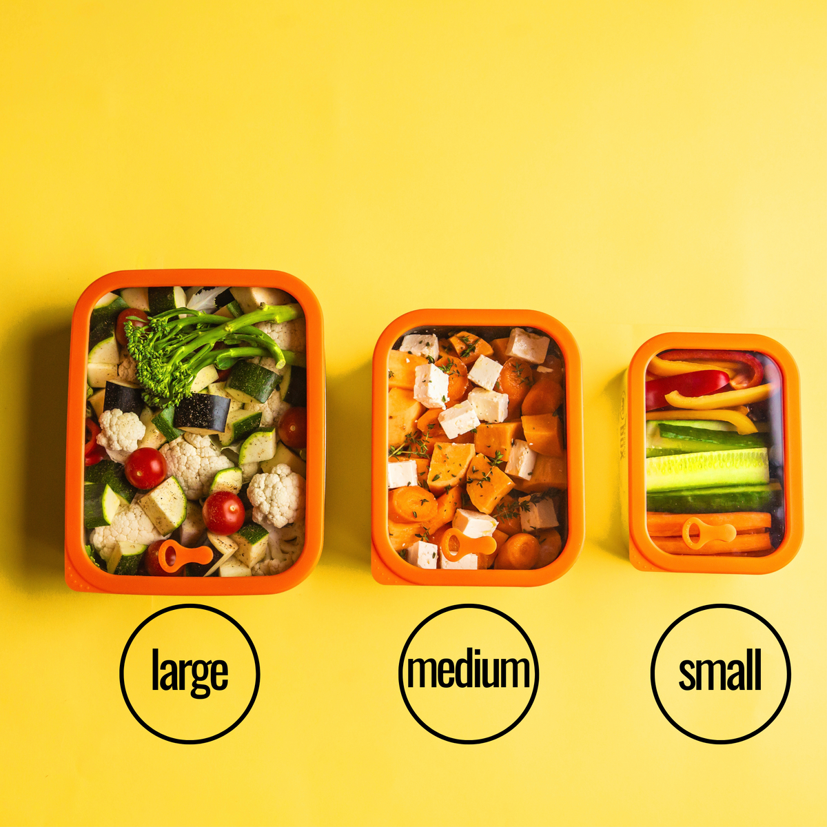 Three metal food containers labeled 'large', 'medium', and 'small' filled with various vegetables for meal prepping on a yellow background. The glass lid allows you to see the food inside. 