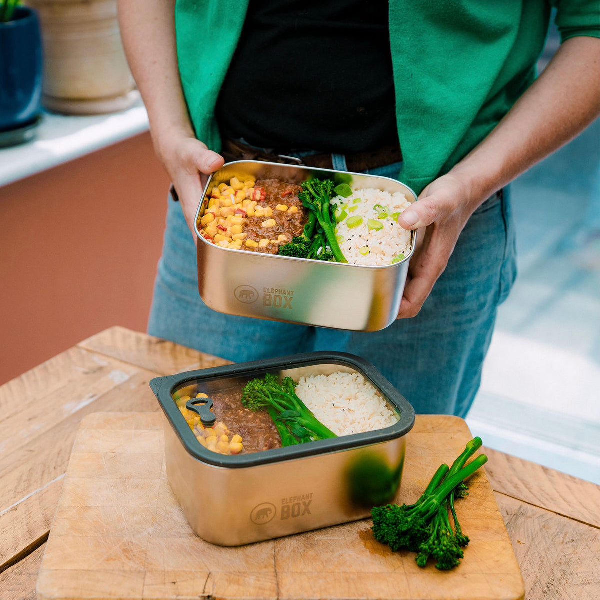 Person holding a stainless steel food container with food on a wooden surface