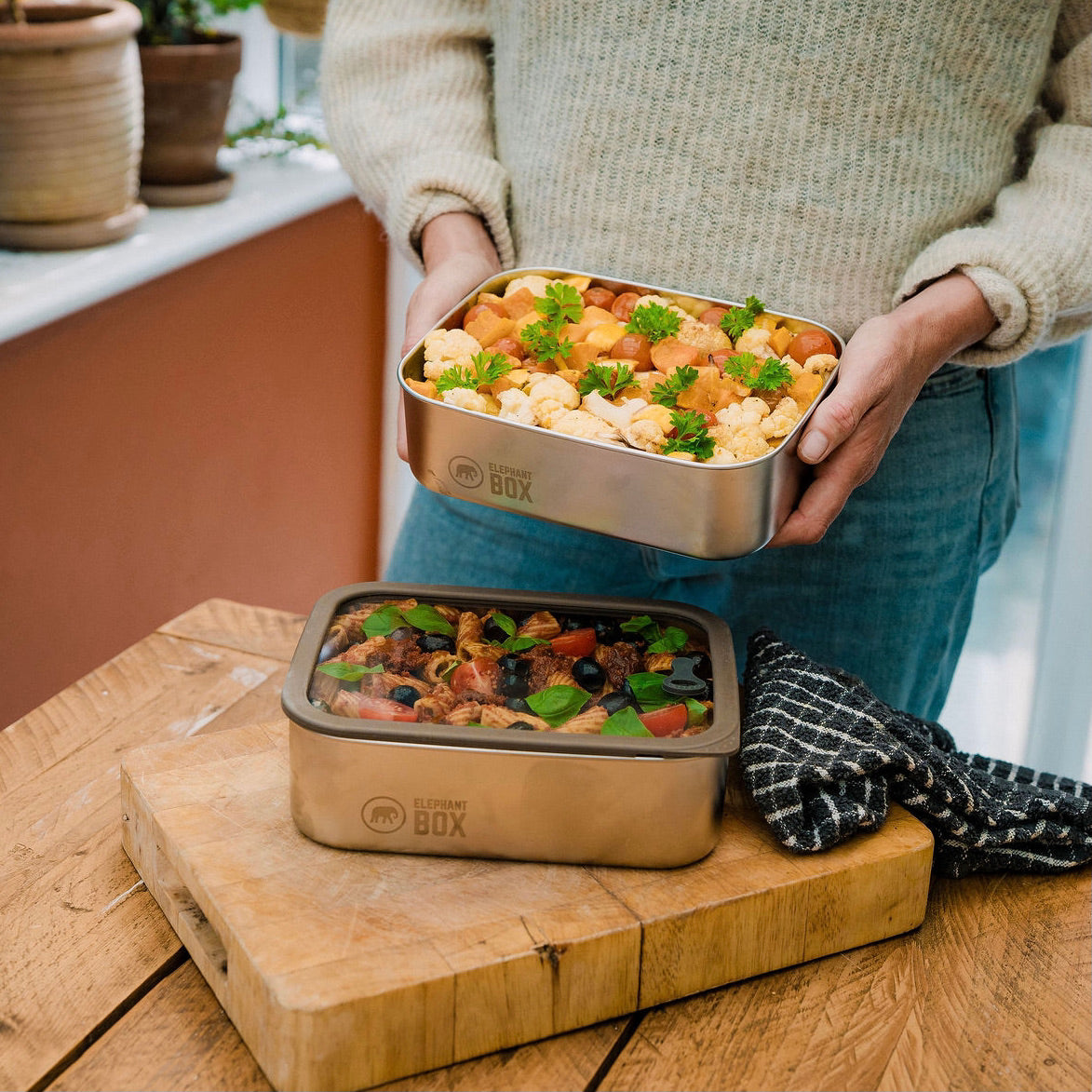 Person holding a metal lunch box with food on a wooden surface
