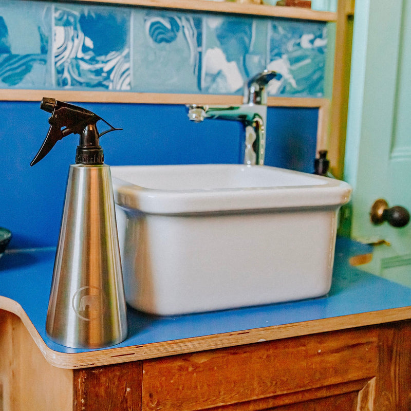 a stainless steel reusable spray bottle next to a bathroom sink 