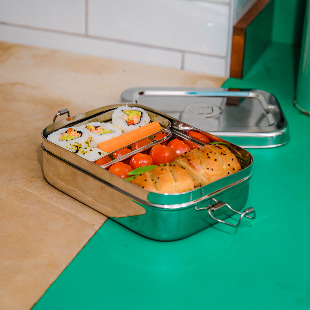 Large stainless steel lunch box with inner snack pod on kitchen counter. 