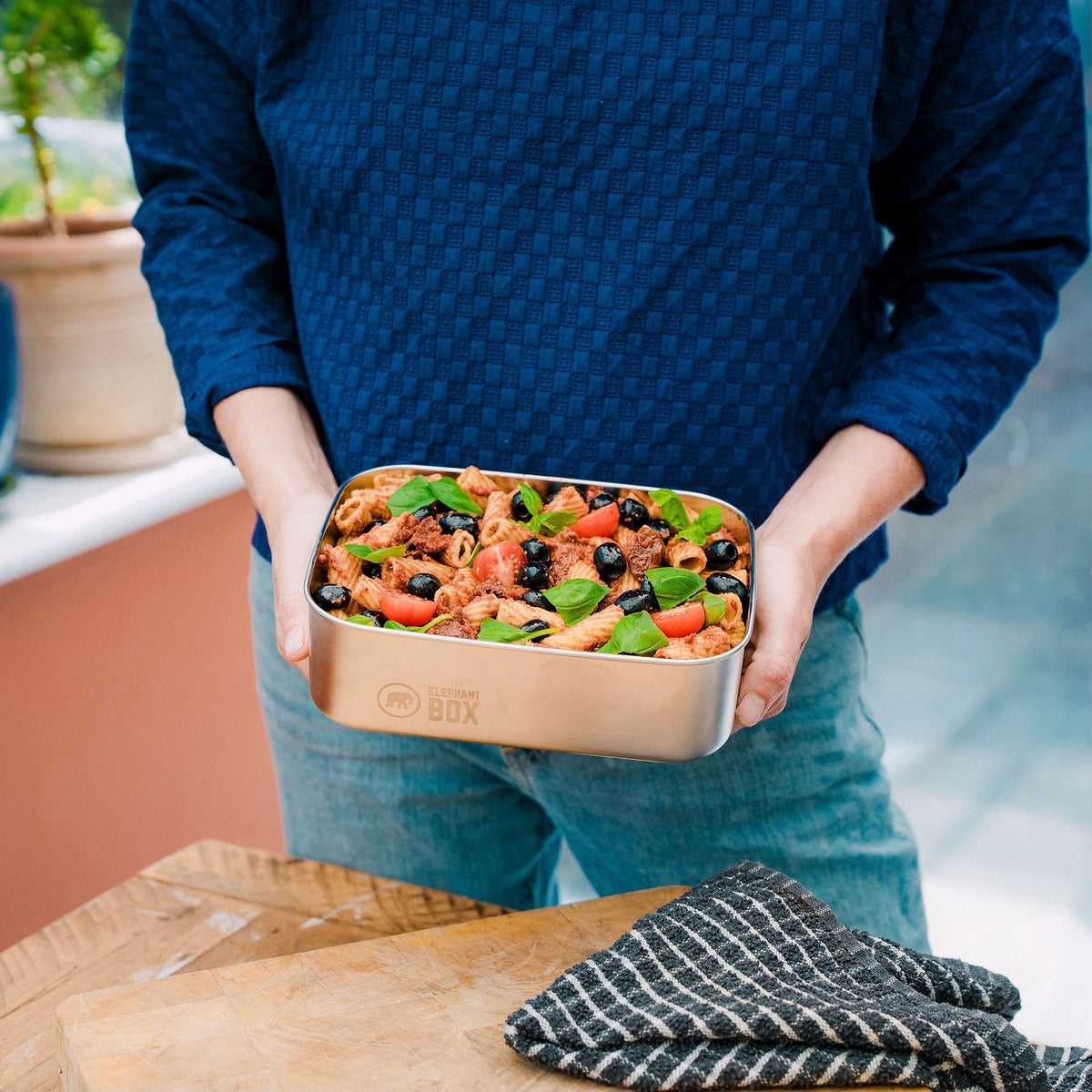 Person holding a metal meal prep box with pasta salad outdoors