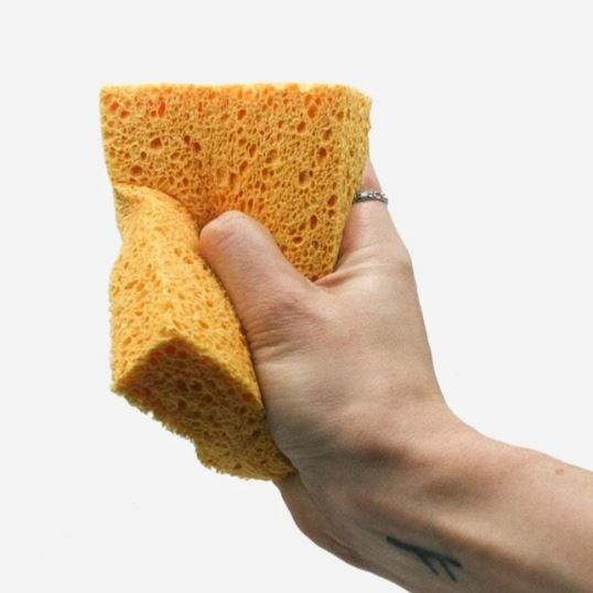 a compostable beige sponge being squeezed in someones hand