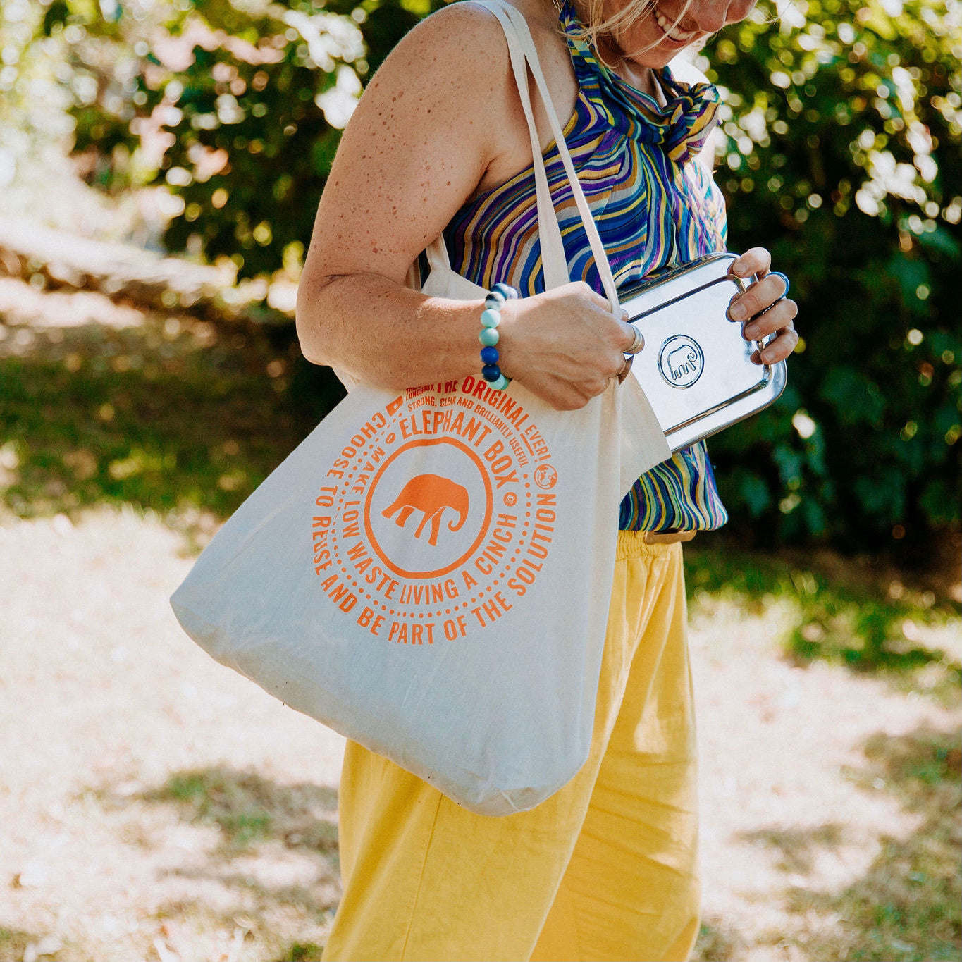 A natural coloured recycled plastic tote bag with orange printed text and an elephant box  graphic on the front.