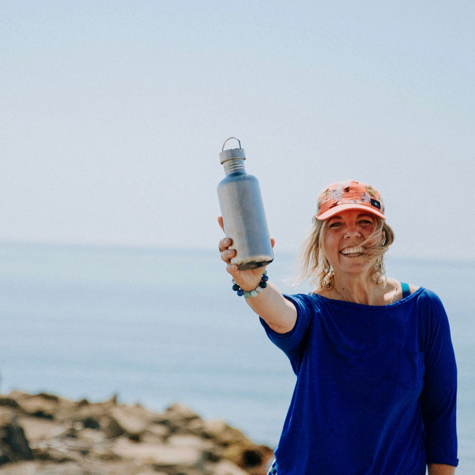 woman holding out an elephant box large metal single wall water bottle with a 100% stainless steel construction and a carry loop with a wide mouth and screw top lid. 