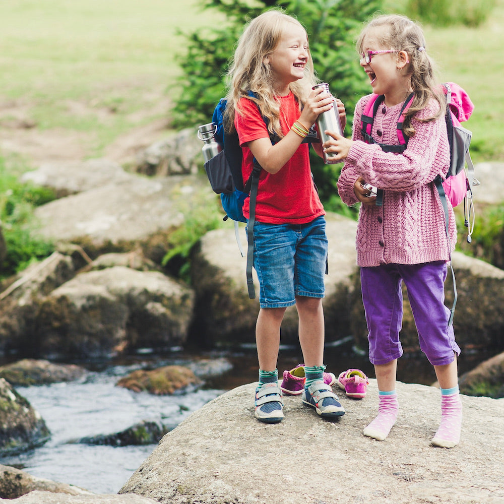 two young girls standing near a river passing a 750ml single wall stainless steel bottle between them 