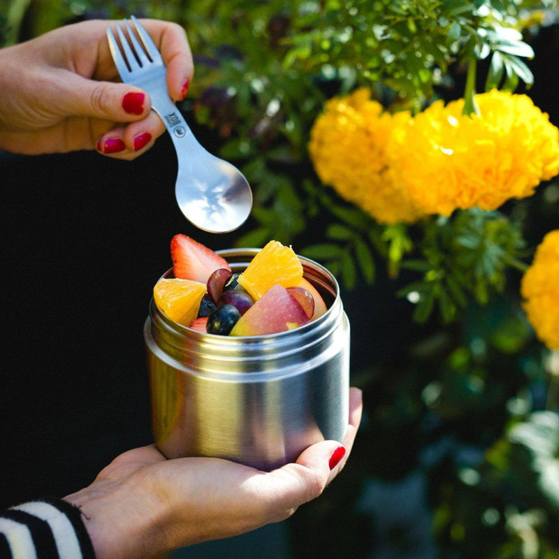 a elephant box leakproof stainless steel food canister with a screw top lid being held by a woman and containing  a fruit salad 