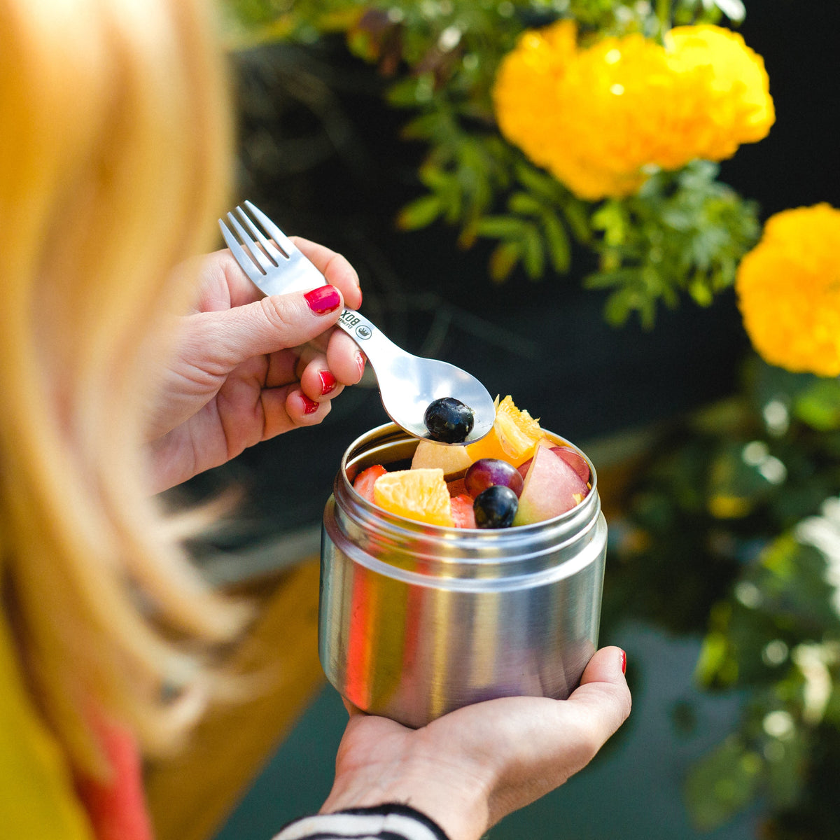 A person is holding the medium metal food storage container  filled with assorted fruits. The container is round and has a brushed steel finish.